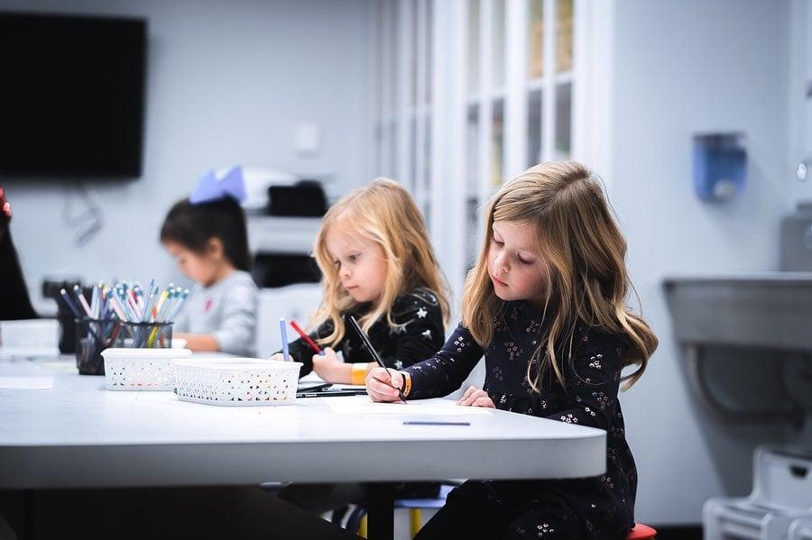 Two girls sitting at a table while drawing.