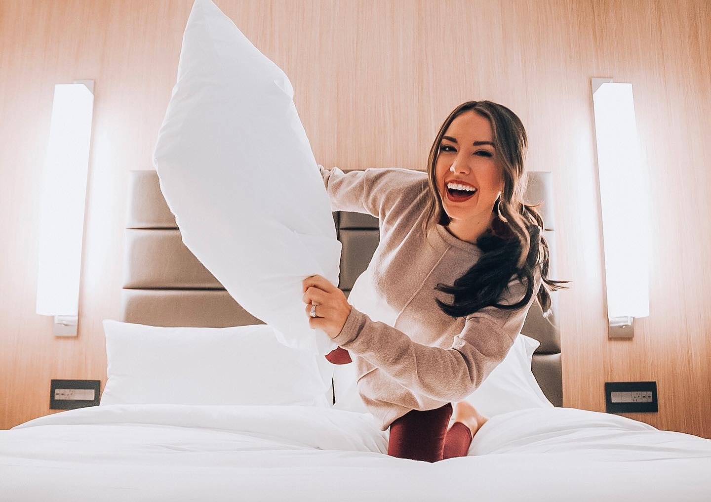 A woman jumping on the bed with the pillow