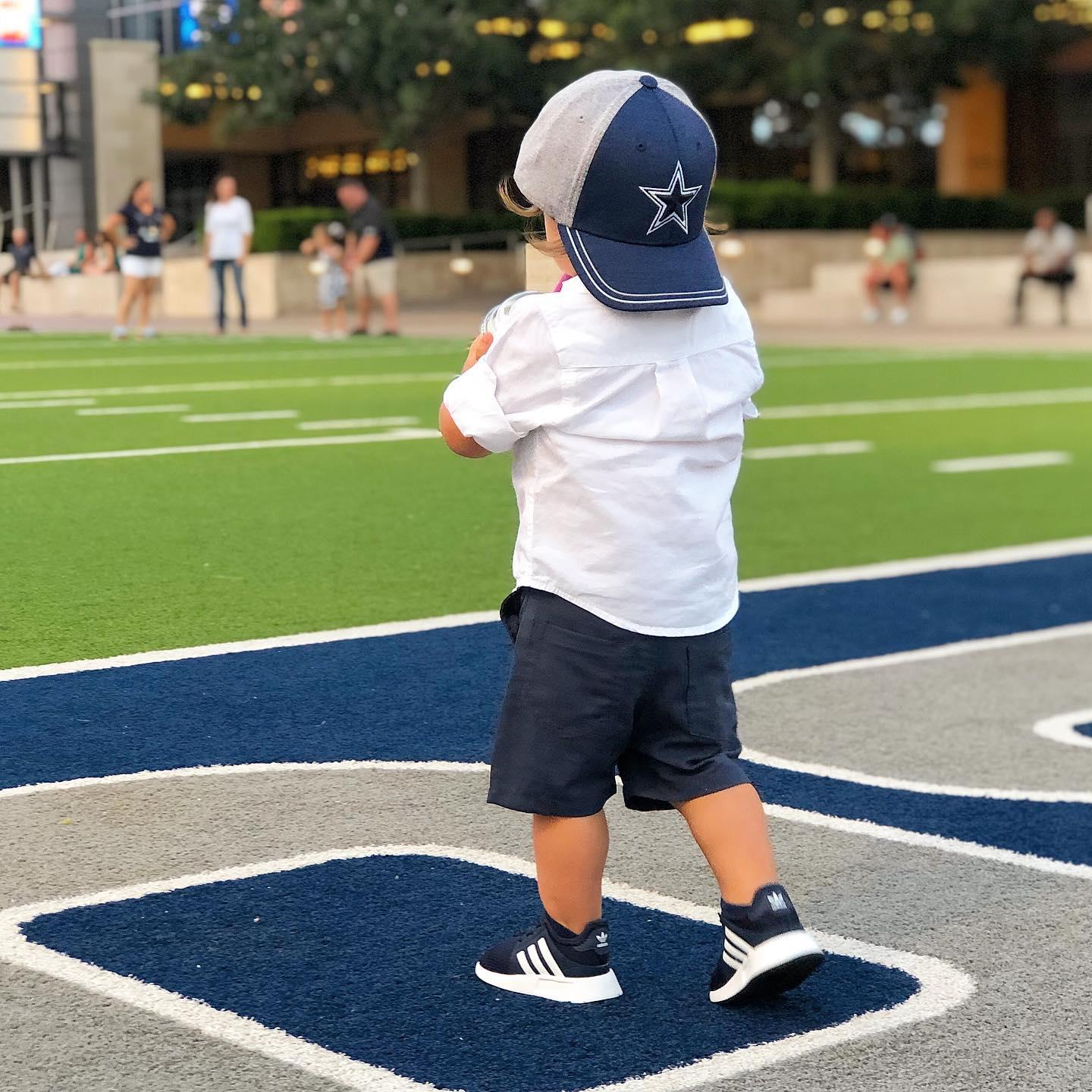 a little boy in a Dallas Cowboys hat standing on a football field