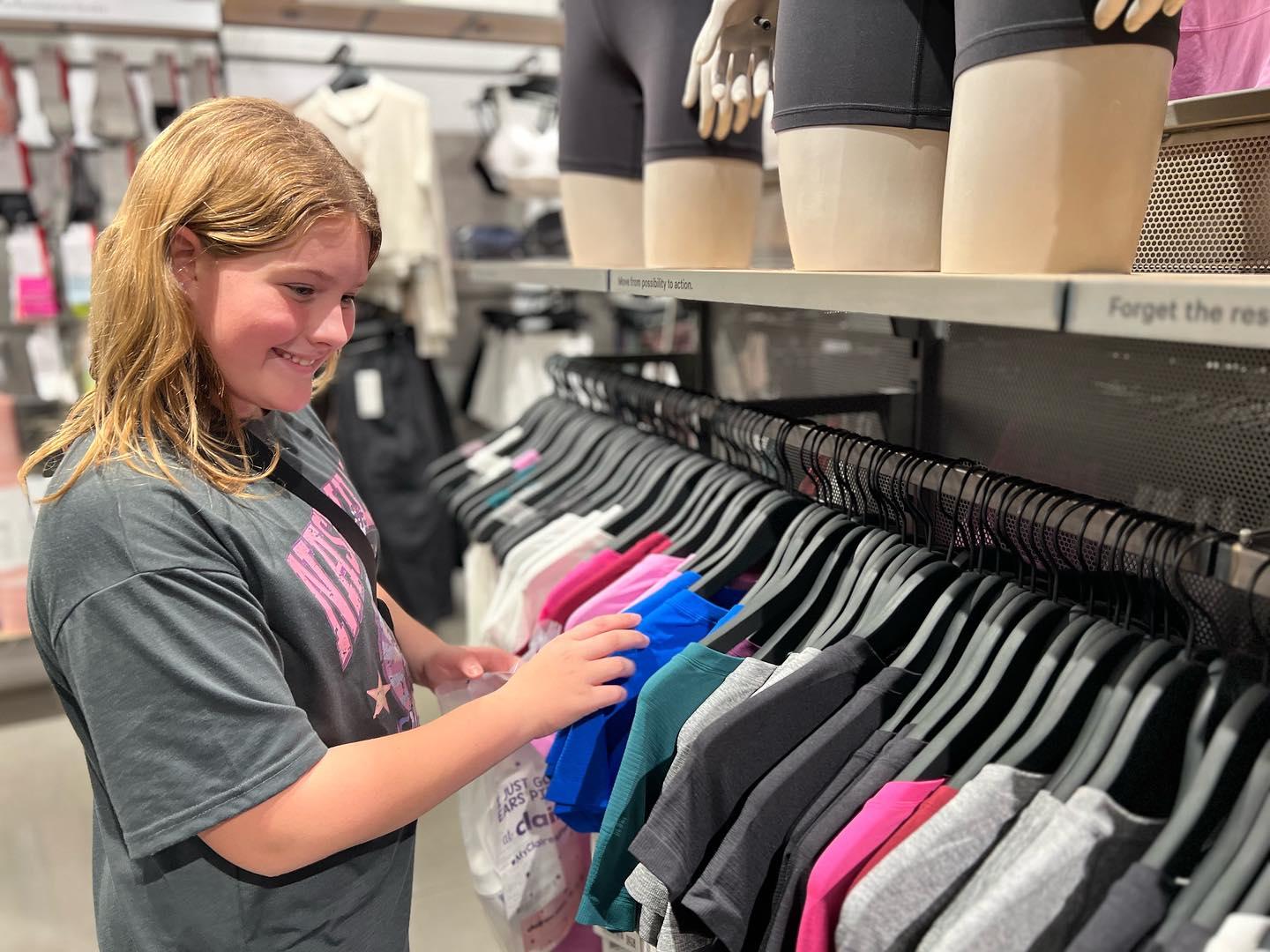 A young girl looks through assorted t-shirts on a clothing rack at a boutique store.