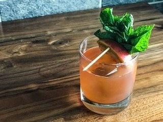 A cocktail with a generous mint garnish on a wooden table.