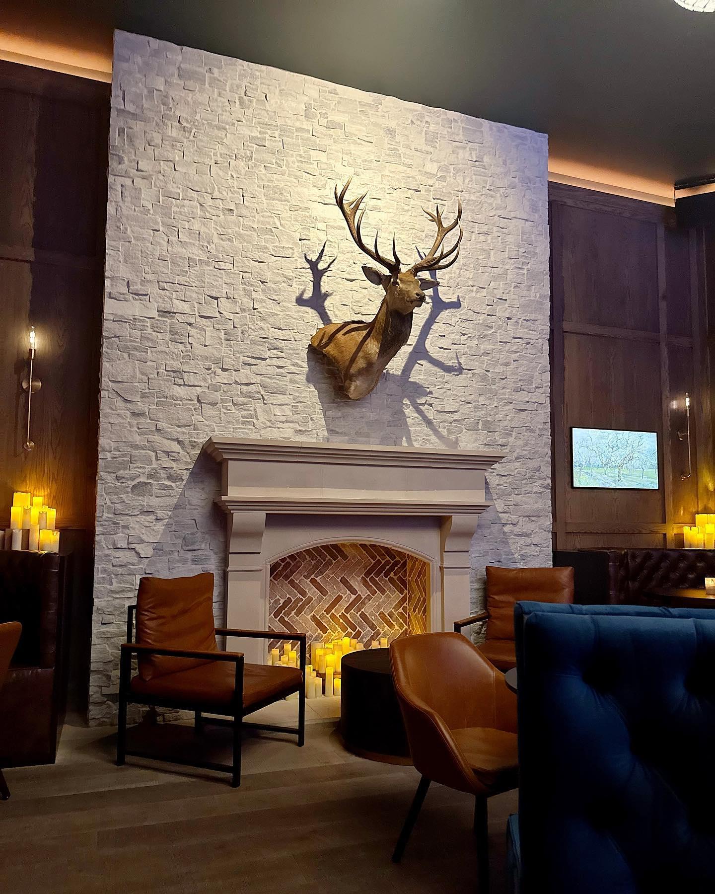 A cigar lounge with leather arm chairs in front of a fireplace and a stag head mounted above the mantel.