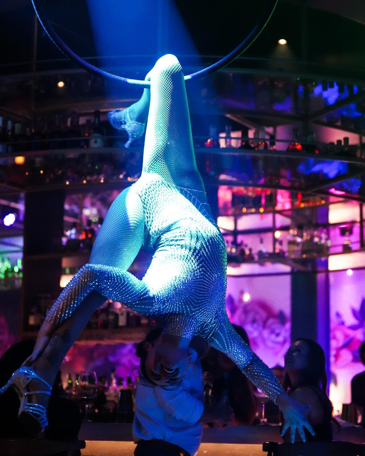 A woman in a sequinned outfit performs an acrobatic routine in dramatic lighting.