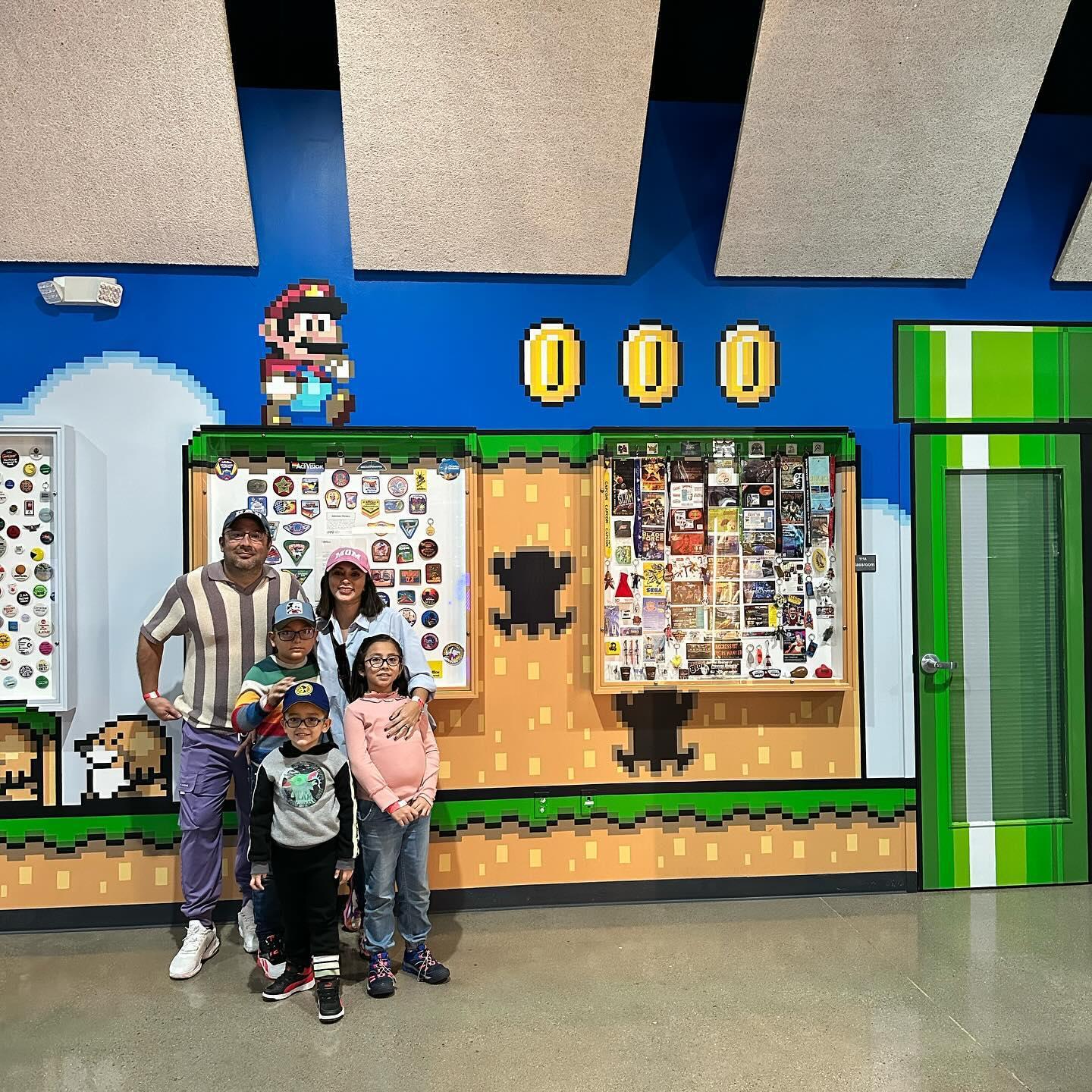 A mother, father and two children pose for a photo in front of a colorful Mario exhibit.