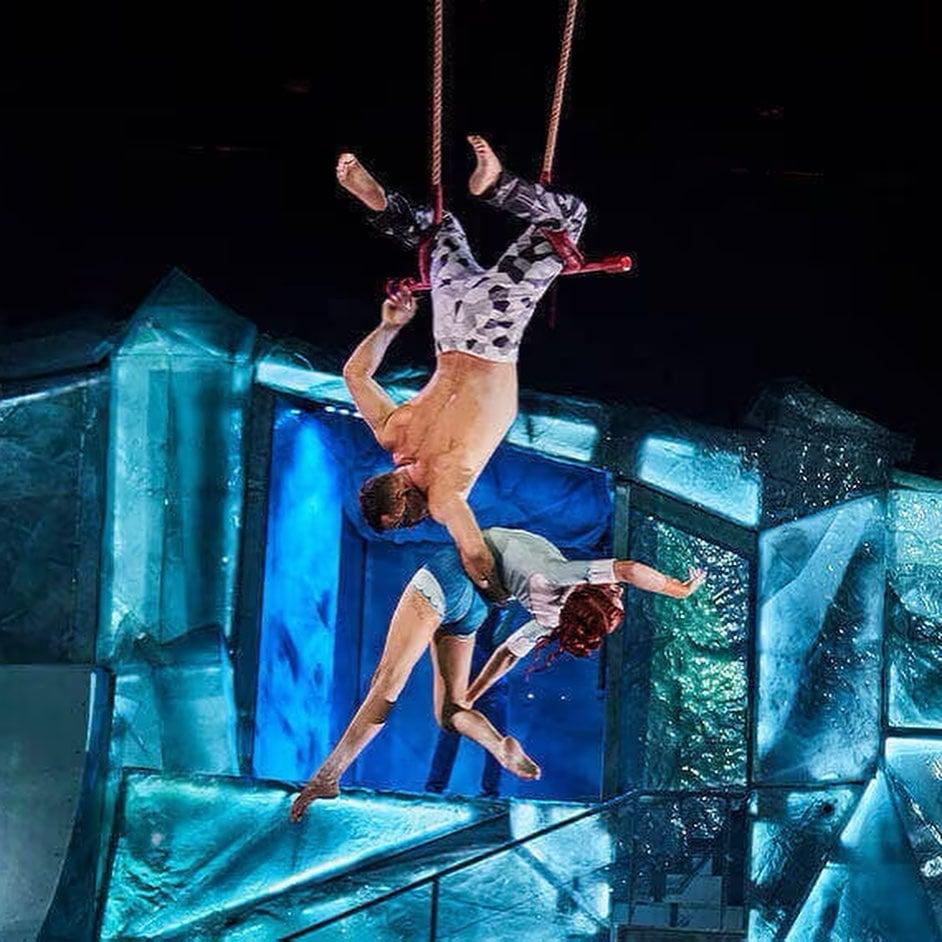 Circus performers do an acrobatic routine with dramatic black and blue lighting.