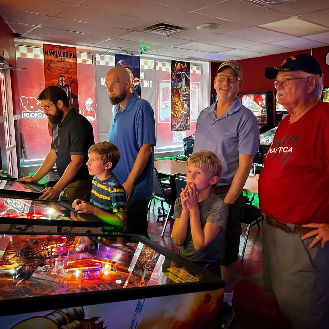 A family plays on pinball machines in a game room.