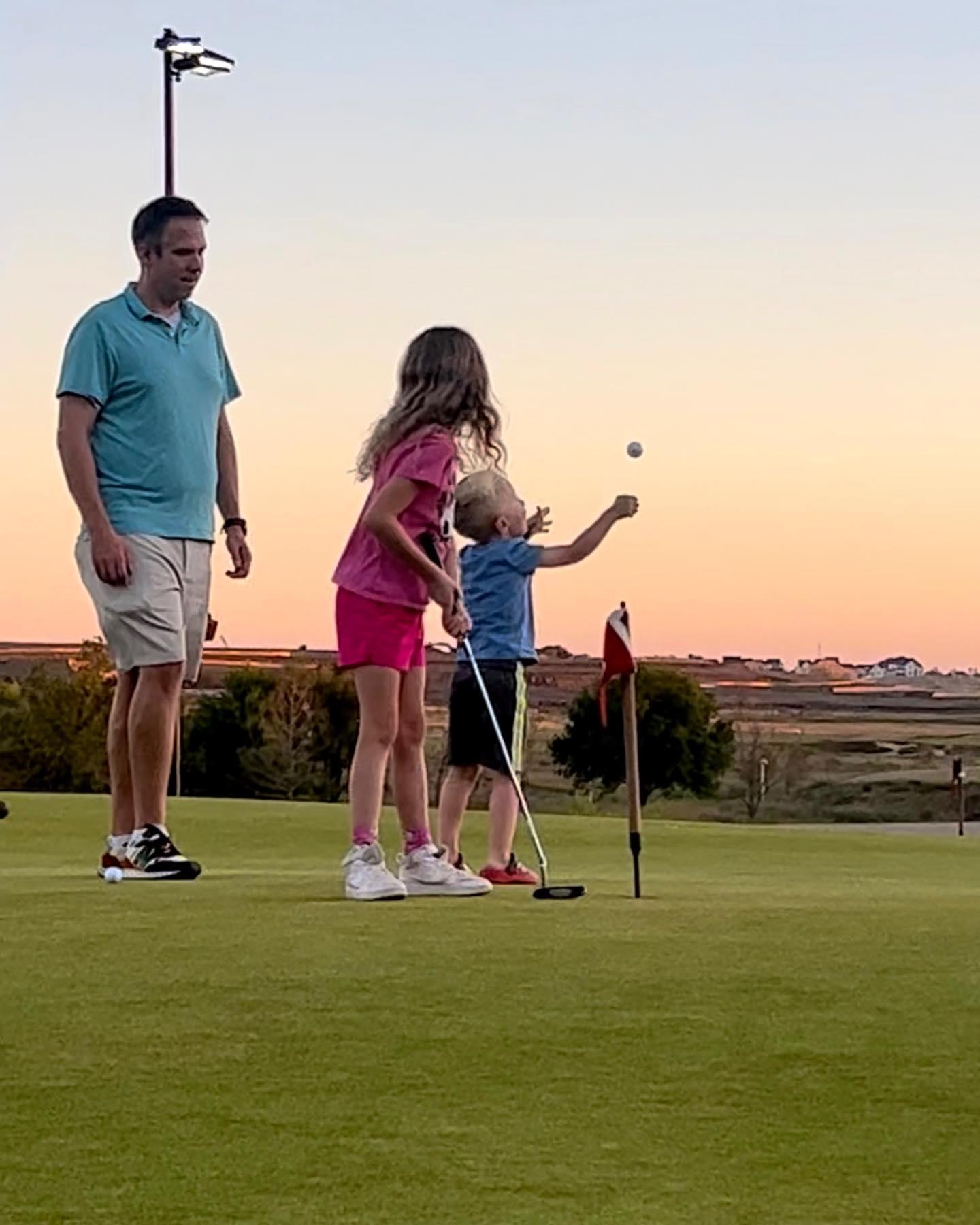 A family plays golf at sunset.