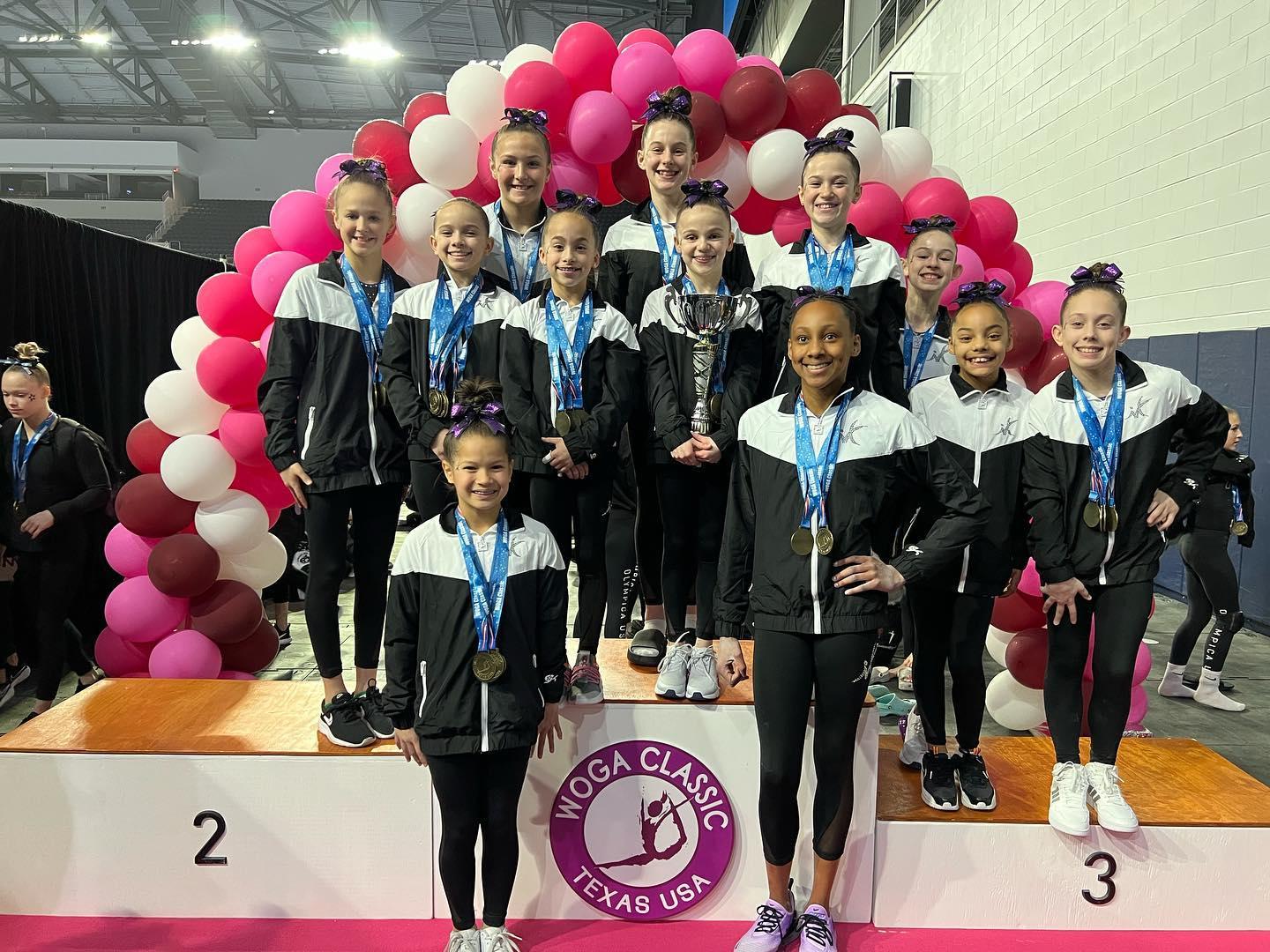 A group of gymnasts pose at an award podium.