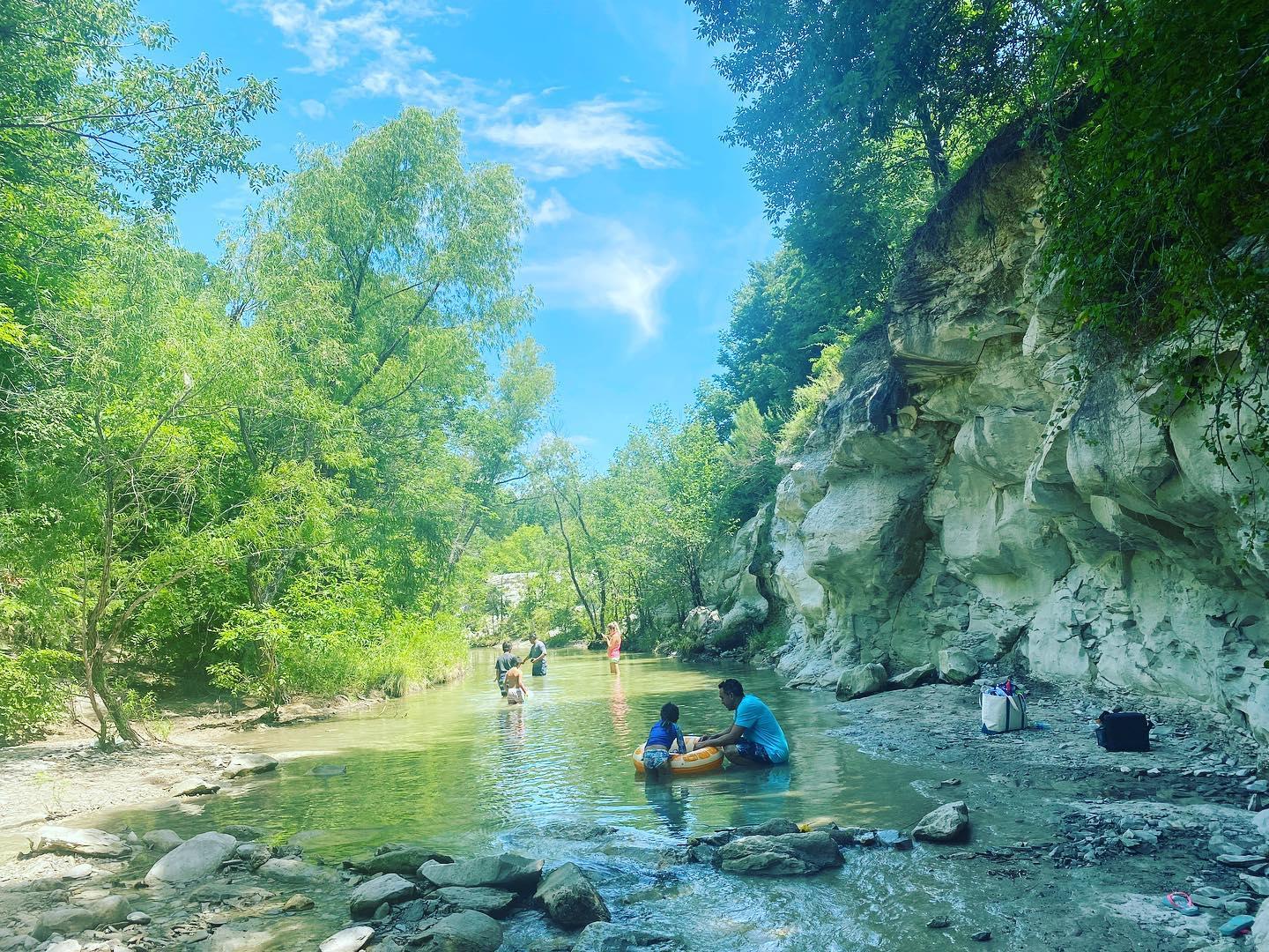 A few people play in a shallow body of water in a quarry on a sunny day.