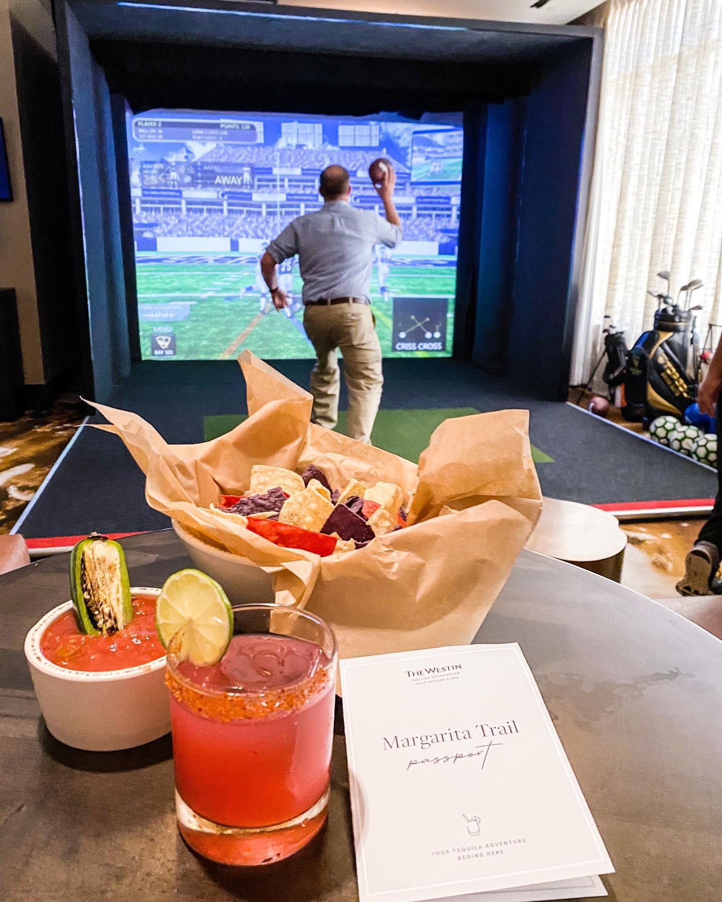 A cocktail and nachos and salsa, a golf simulator in the background.