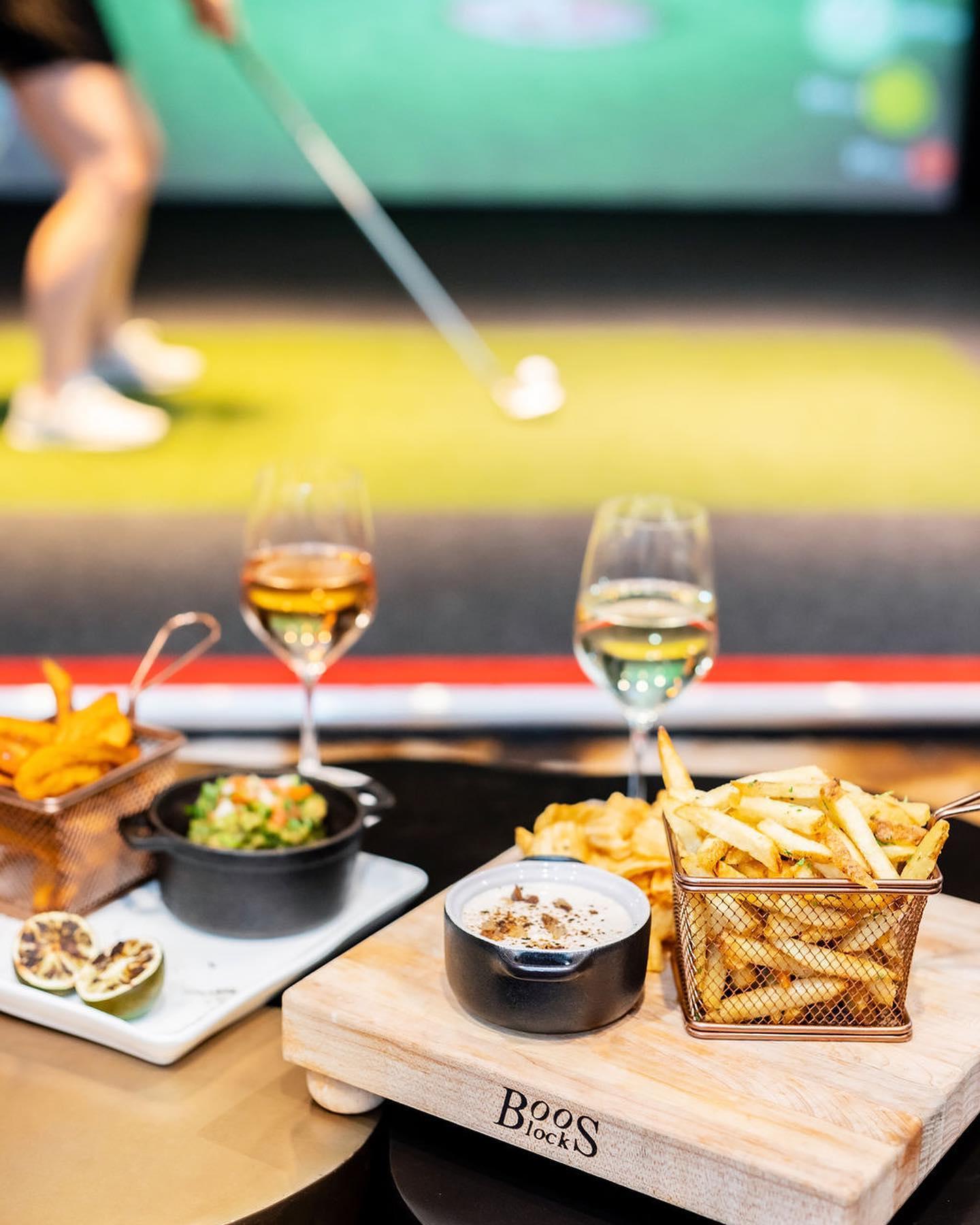 Fries and glasses of wine with a golf simulator in the background.
