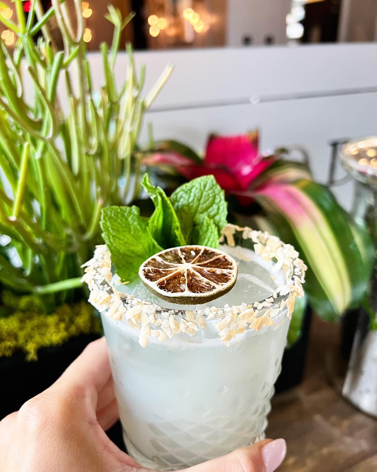 A manicured hand holding a margarita with a dried lime garnish.