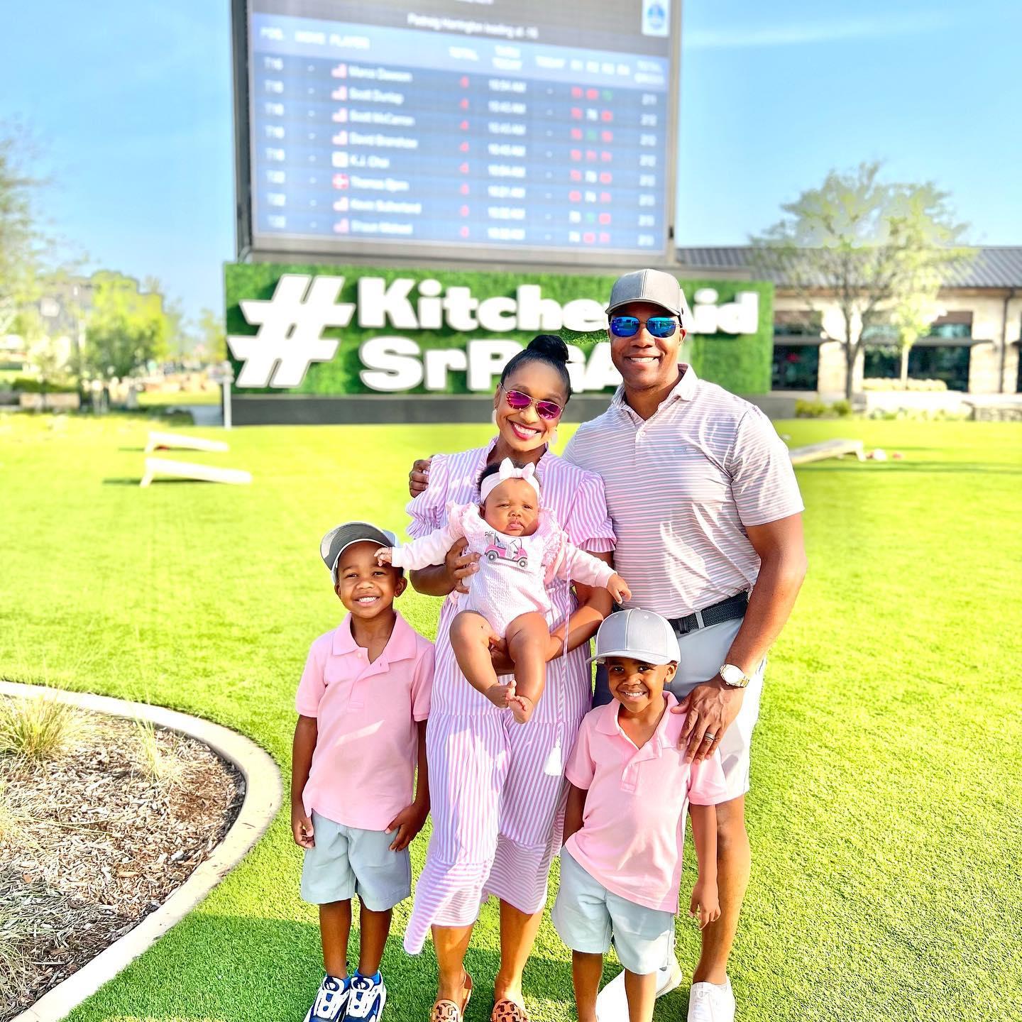 A family poses for a photo on a golf green. They are wearing matching pink golf outfits.