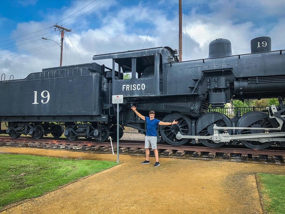 A man poses in front of an old steam engine train.