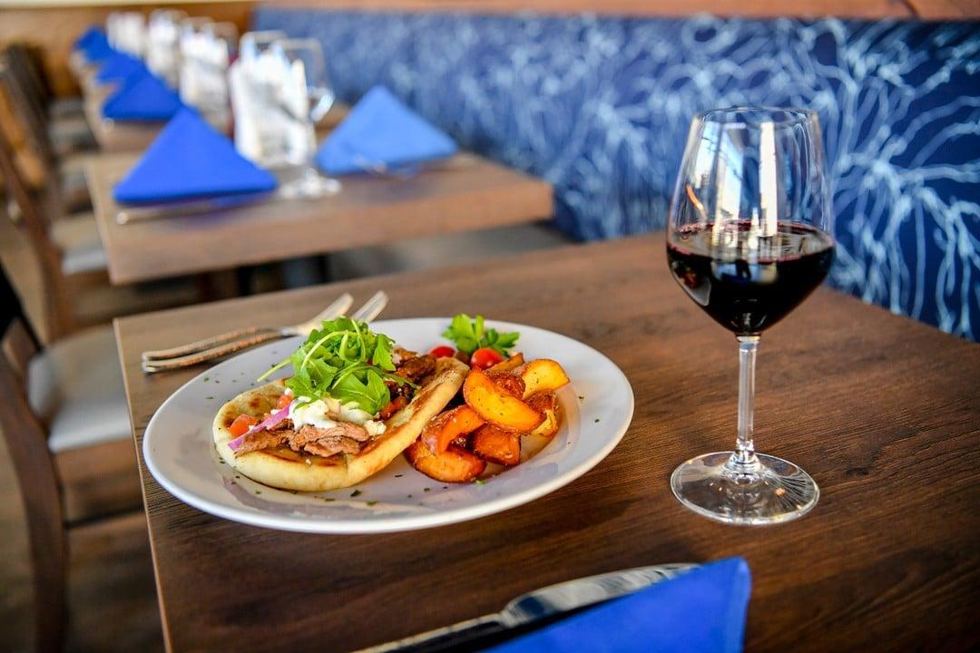 A glass of red wine and a greek pita dish with meat and salad.
