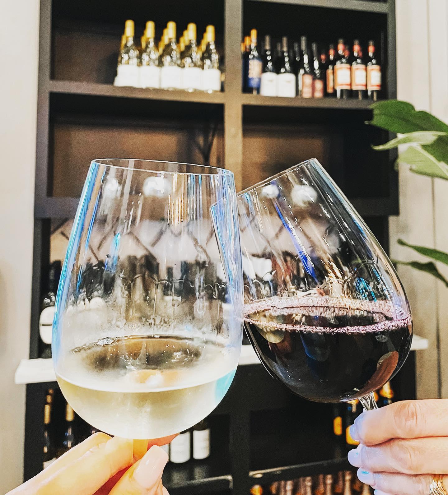 Two hands clink wine glasses, one with red wine and the other with white wine.