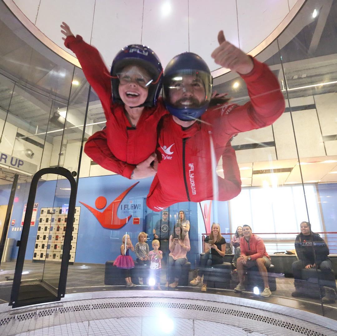 A man and child in a skydiving simulator give thumbs up.