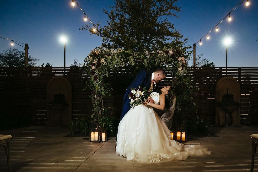 A bride is dipped for a kiss by the groom in a dramatically lit photo area.