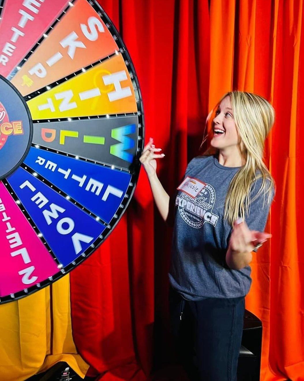 A woman looks excited while she spins a wheel in rainbow colors.