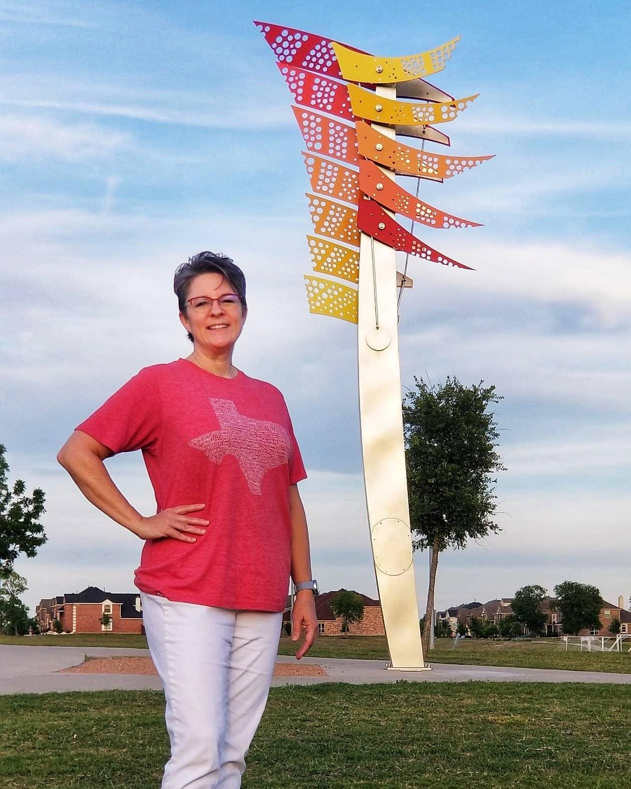 A woman in a pink shirt stands next to a large abstract statue.
