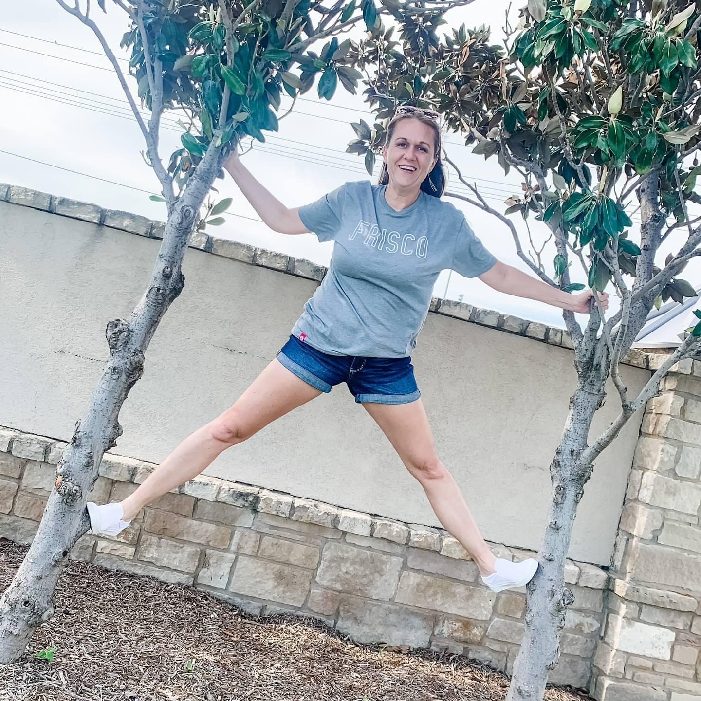 A woman wearing a Frisco t-shirt and shorts balances in the air between two trees.