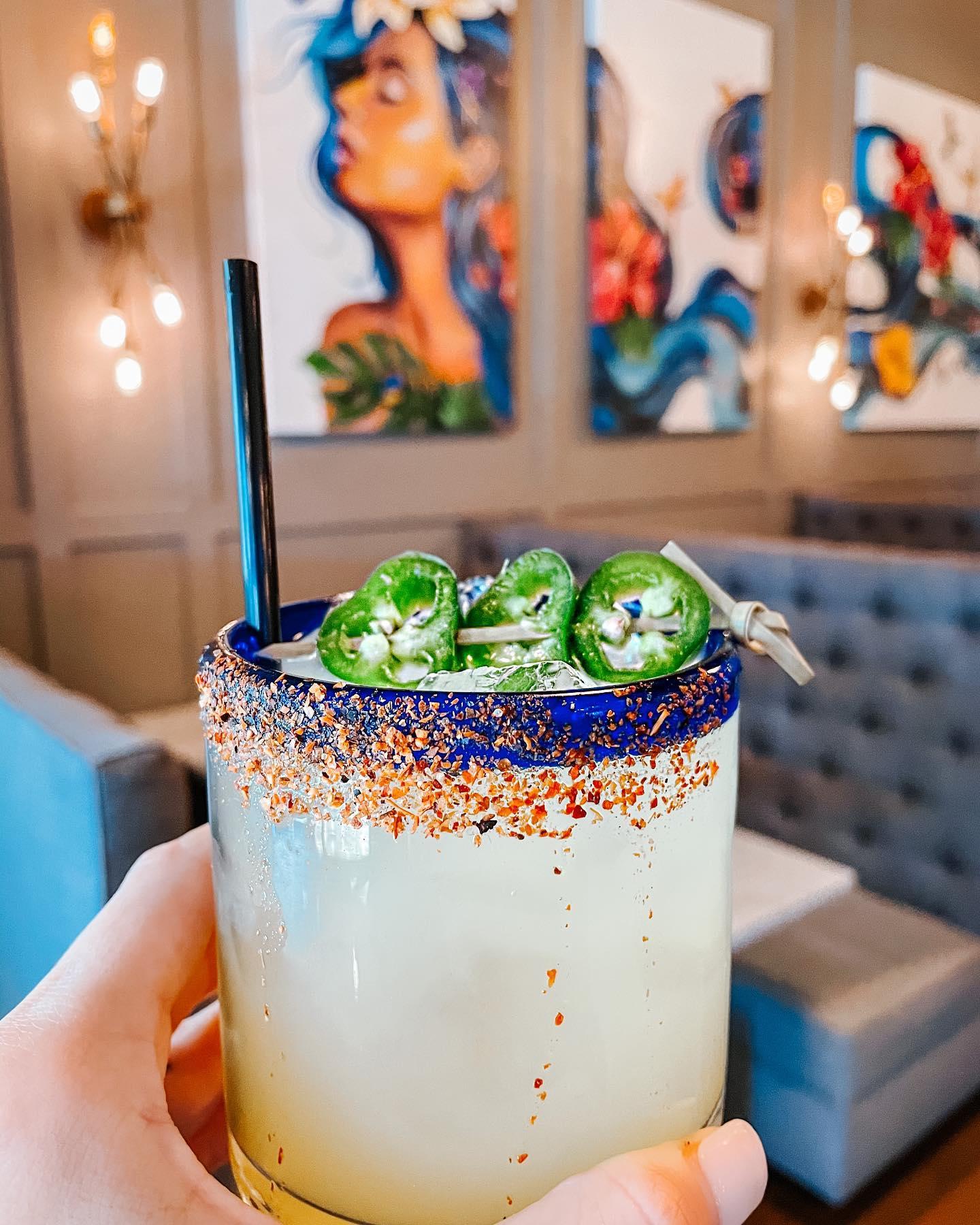 a cocktail in a blue rimmed class with jalapeno garnish