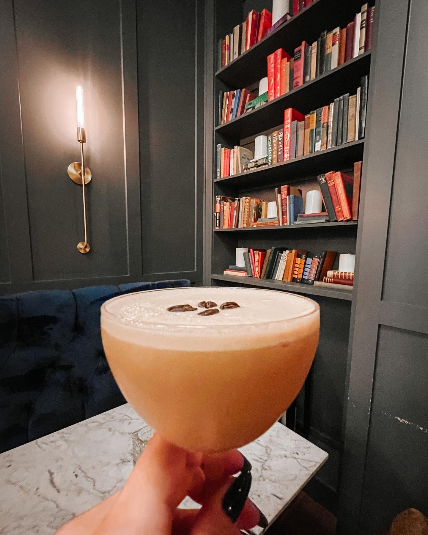 a woman enjoying an espresso cocktail in a library like environment