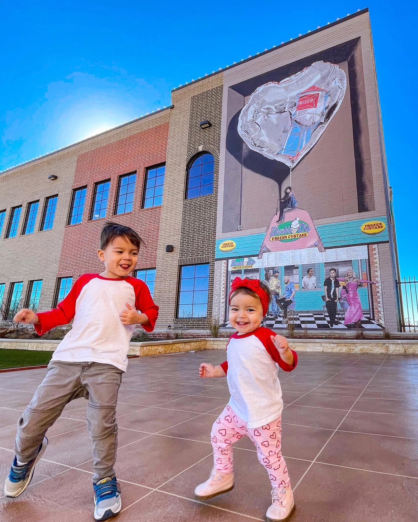 two kids dancing in front of a mural