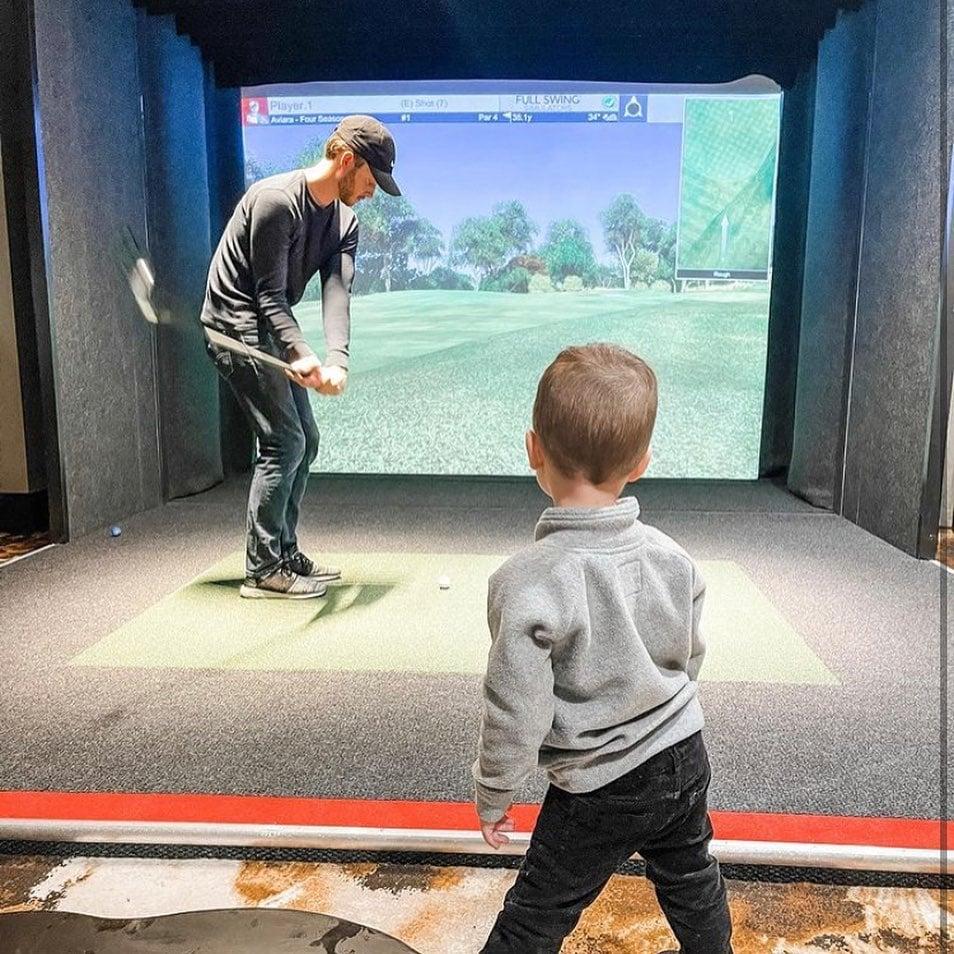 A dad and son playing a golf simulator