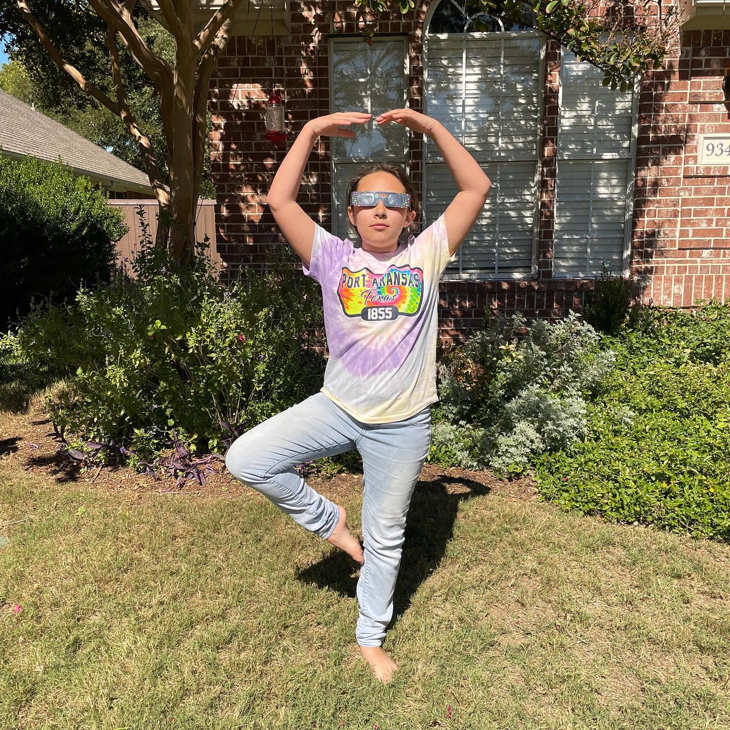 a child standing in tree pose wearing eclipse glasses