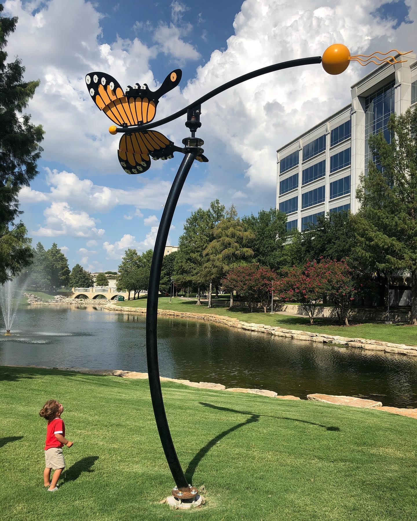 A little kid looking up at a sculpture of a butterfly