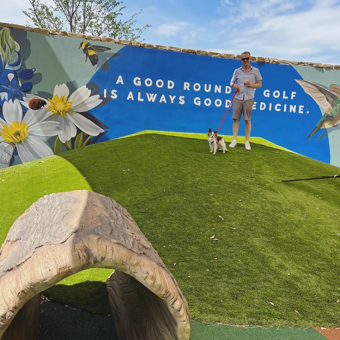 a man standing on a hill with his dog in front of a mural