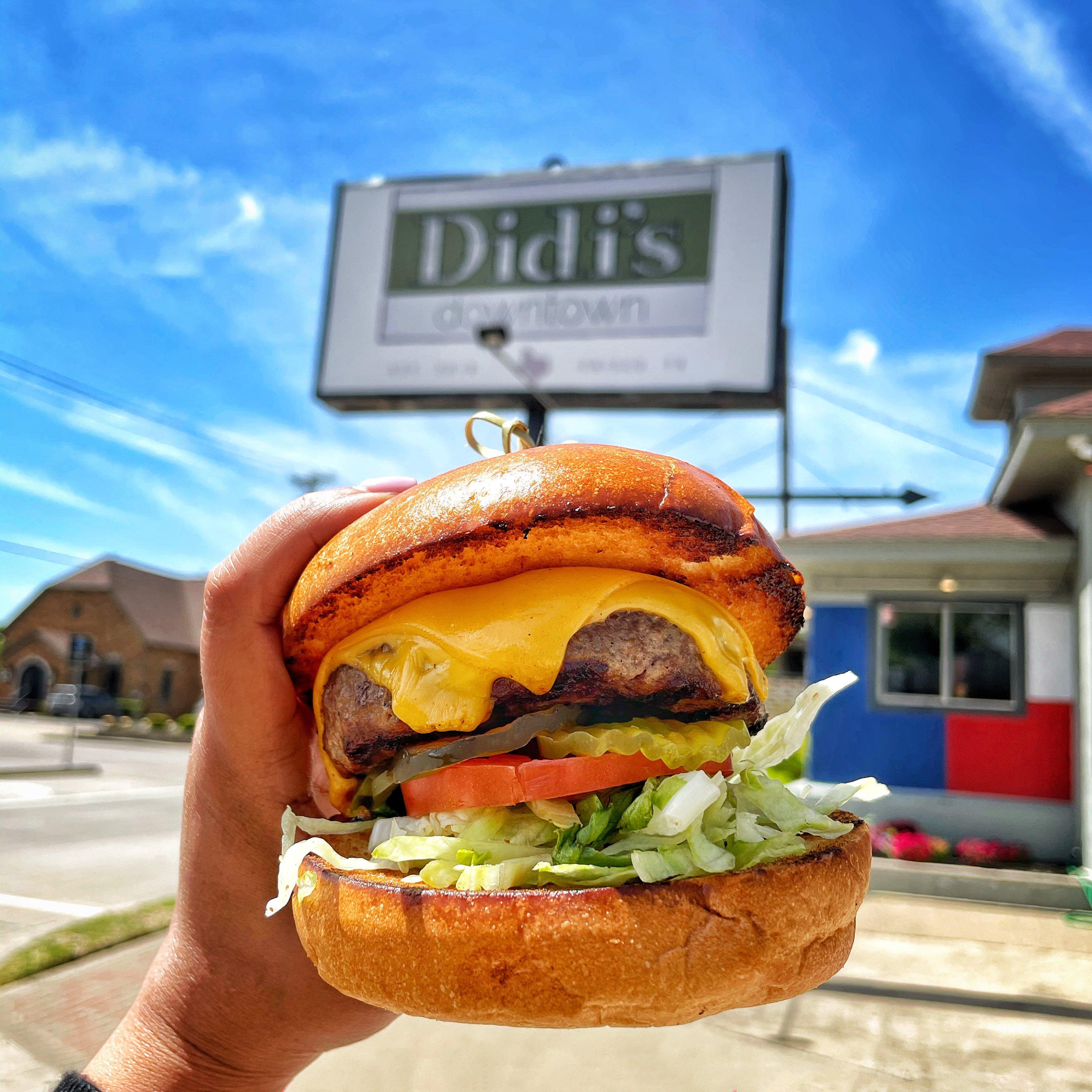 a person holding a large burger under the Didi's Downtown sign