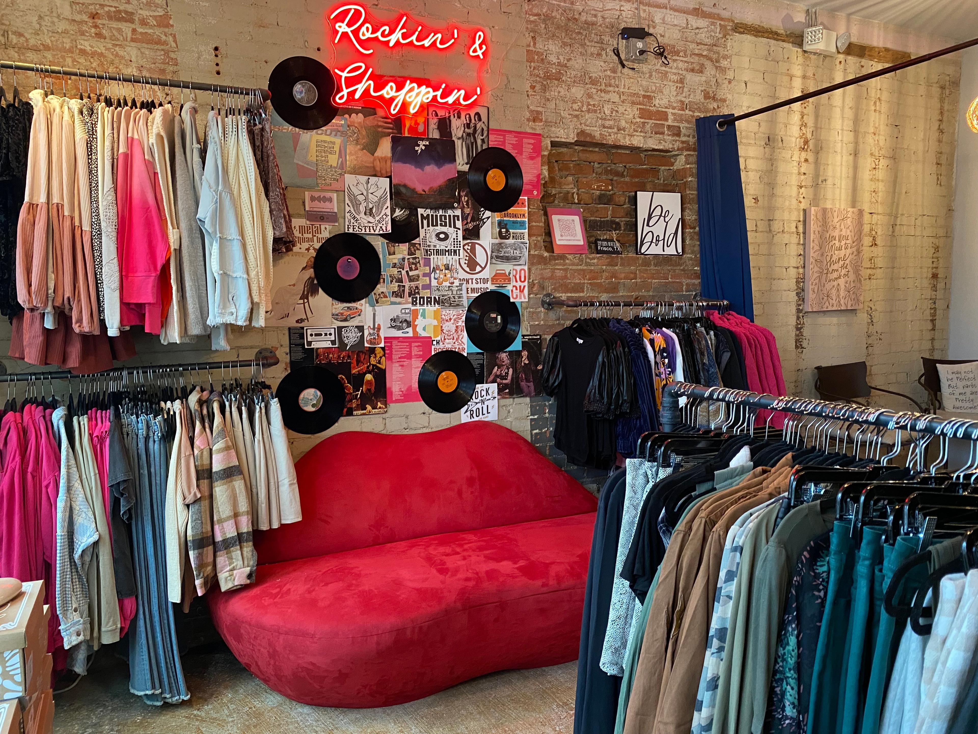 a red couch shaped like lips between clothing racks at a boutique