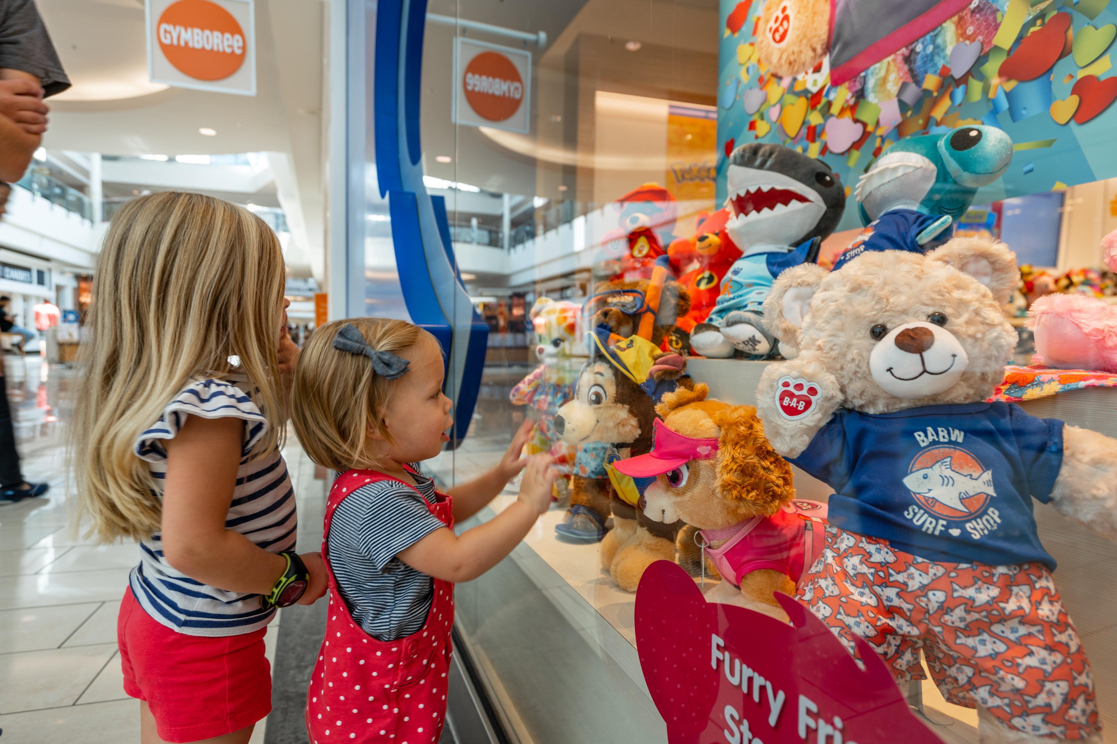 two little girls looking at stuffed animals through a window