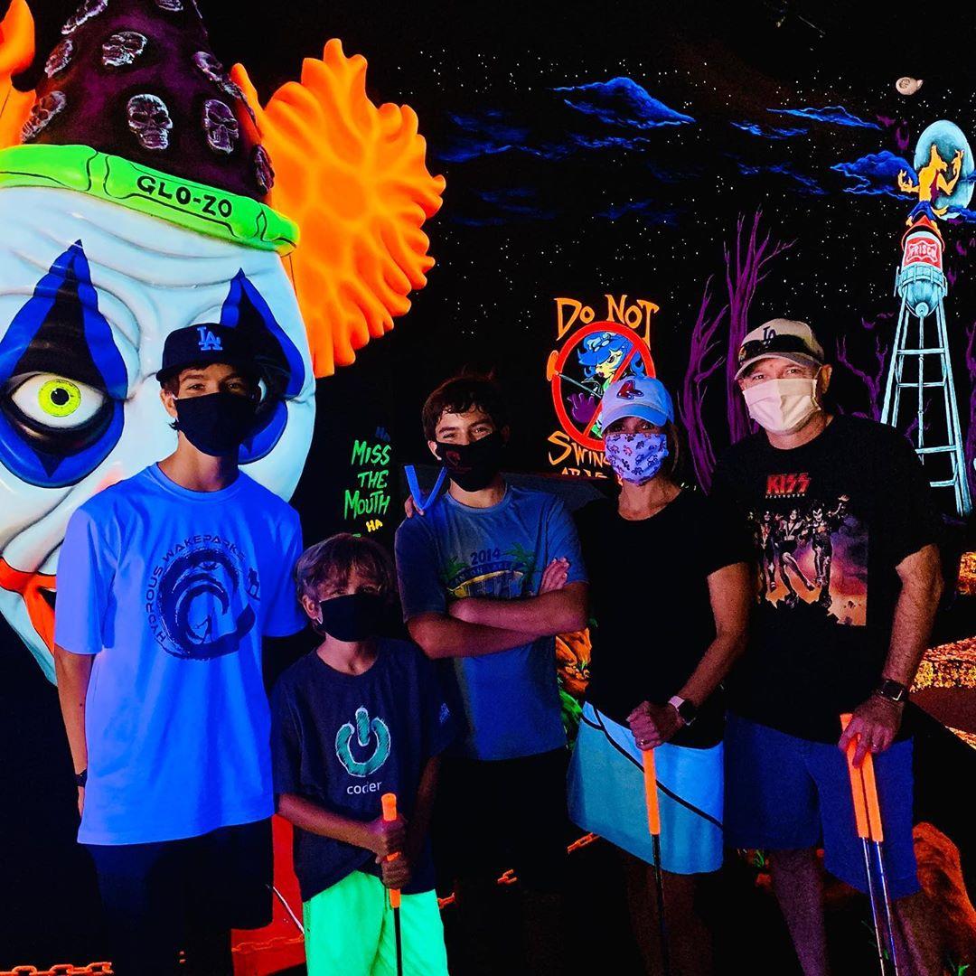 a family in masks posing together in front of a glow in the dark mural while mini putting