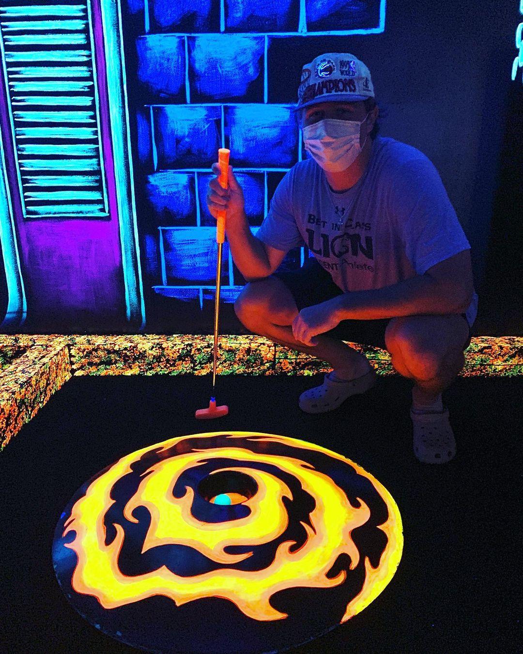 a man standing over a glow in the dark mini putt hole