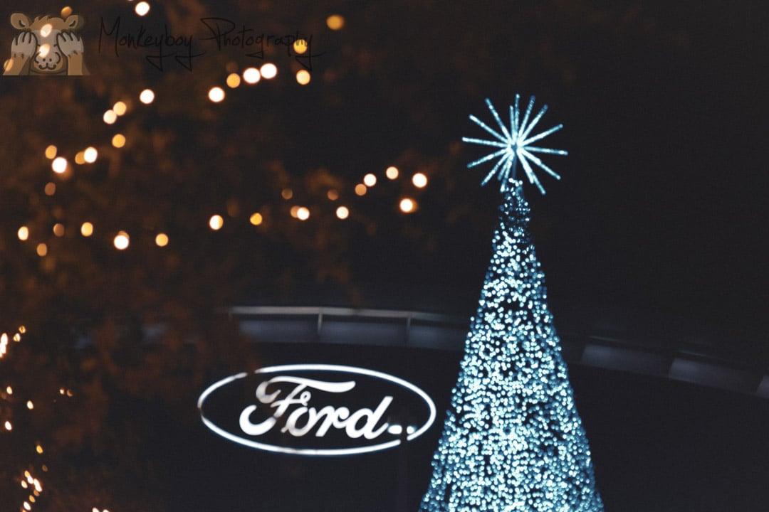 the top of a Christmas tree with white lights next to the Ford Logo