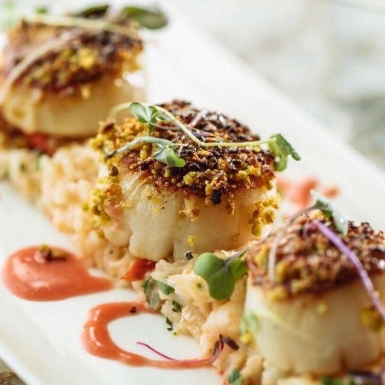 Pistachio crusted seared scallops with lobster risotto and a blood orange butter sauce, topped with micro greens