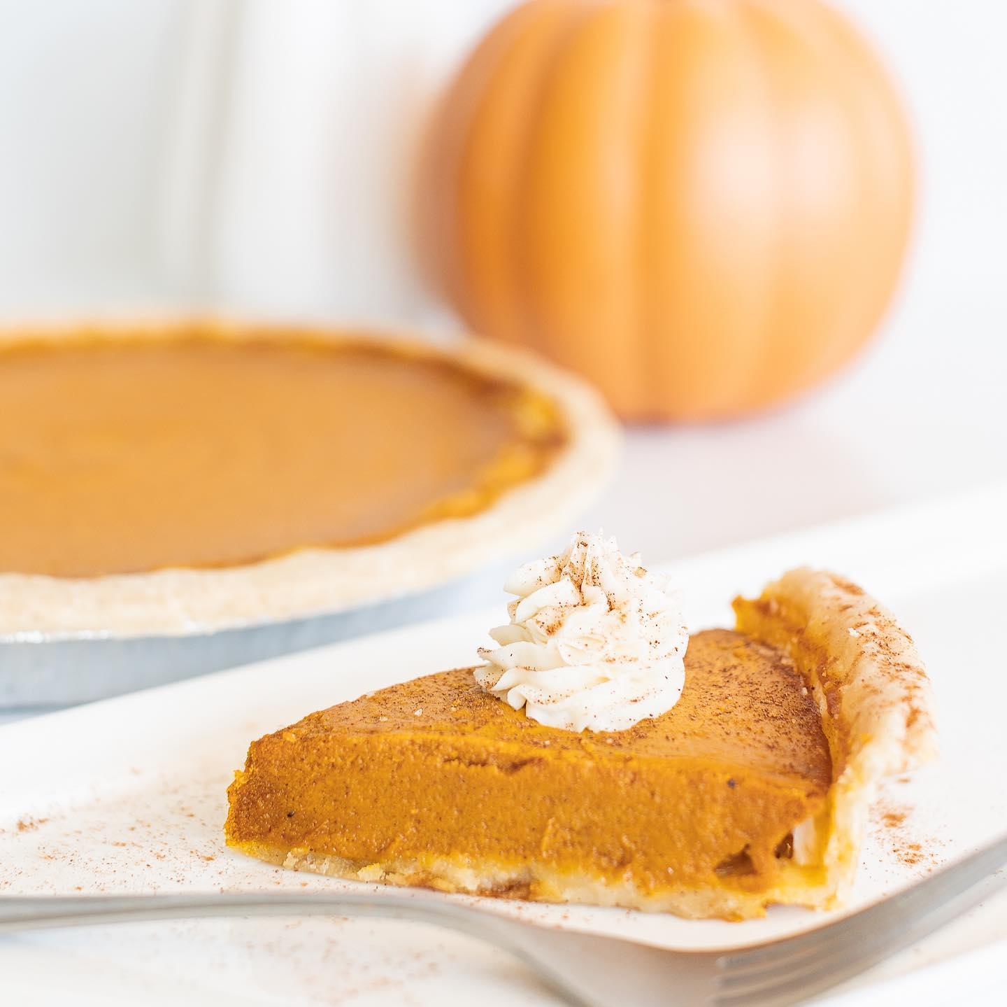 A pumpkin pie and a slice of pumpkin pie with a pumpkin in the background