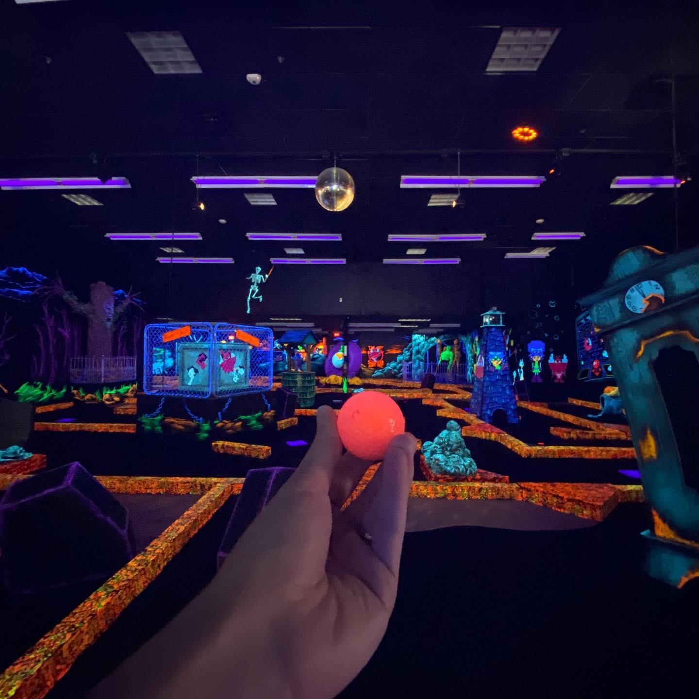 A person holding up a glow in the dark golf ball at mini putt