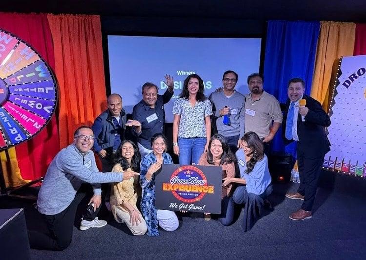 A bunch of people posing for a photo holding a Game Show Experience sign