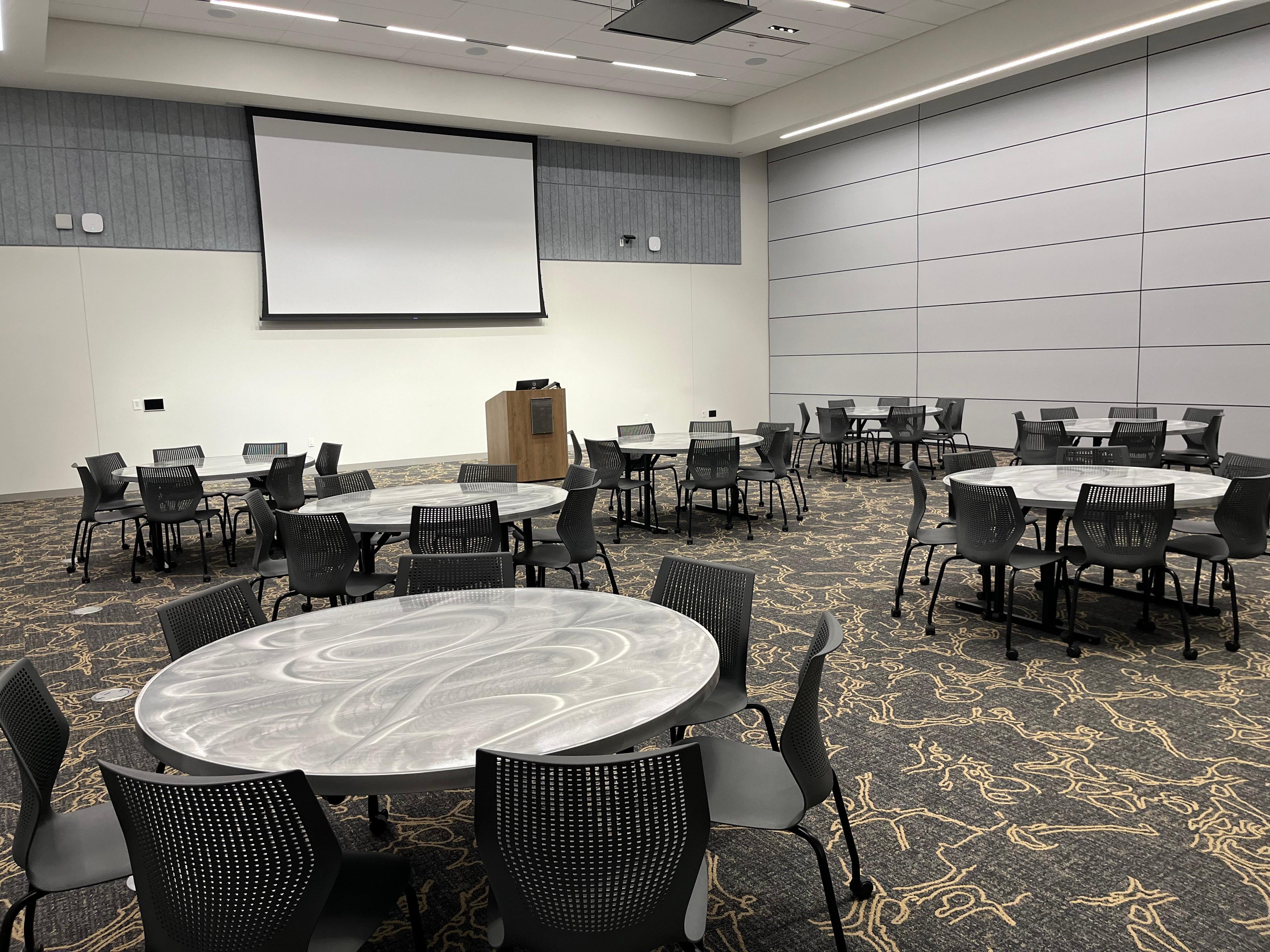 An empty meeting room with round tables and a large screen on the wall
