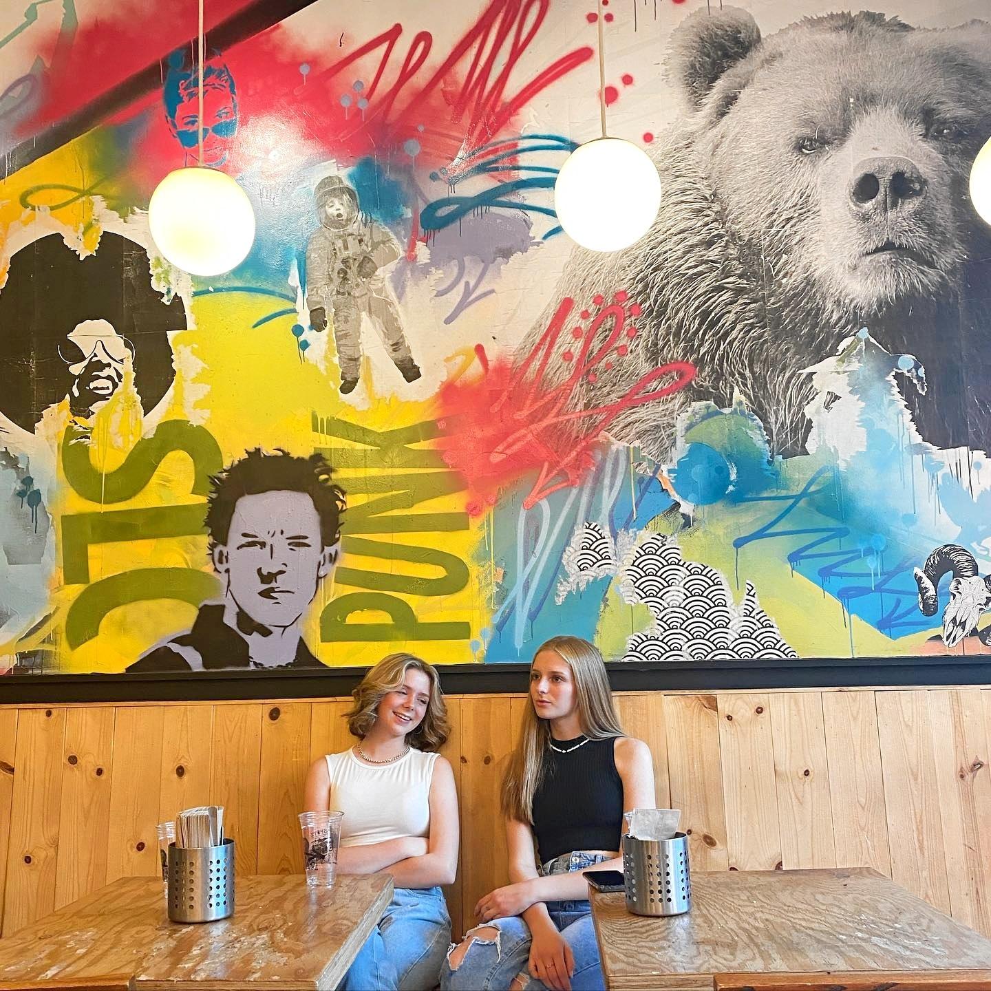 friends sitting in a restaurant that has a large mural on the wall