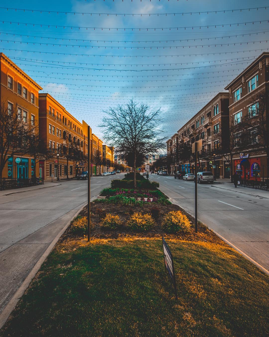 A street with shops and a grassy area between the roads