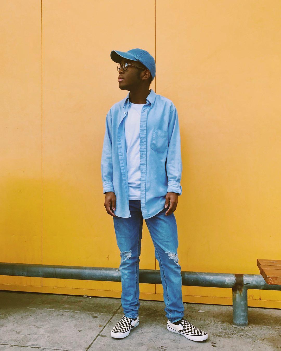 a man in a denim outfit standing in front of the yellow Ikea wall