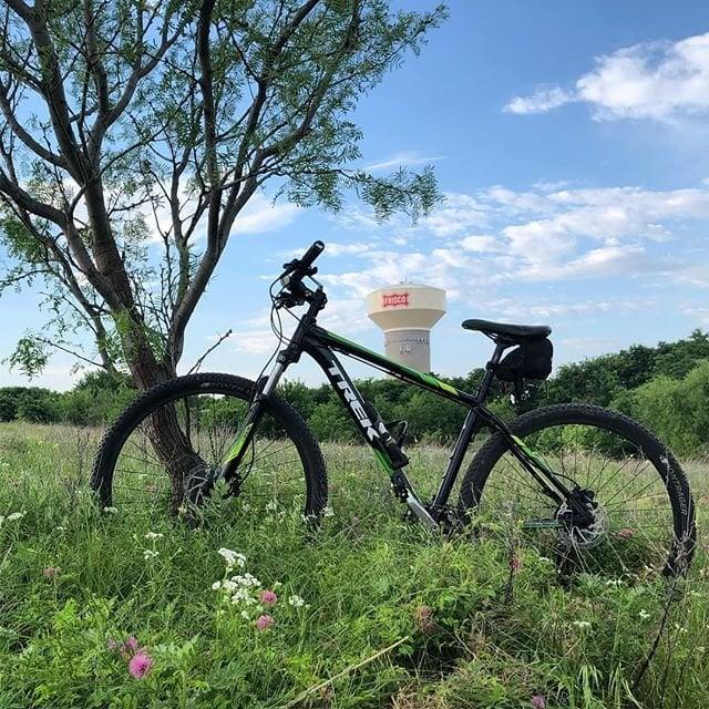 a bike parked by a tree in a field in front of the Frisco water tower