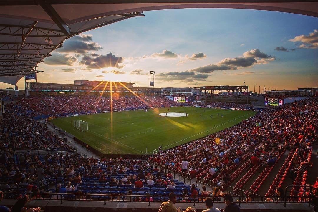 A soccer stadium at sunset. Fans sit in the stands.